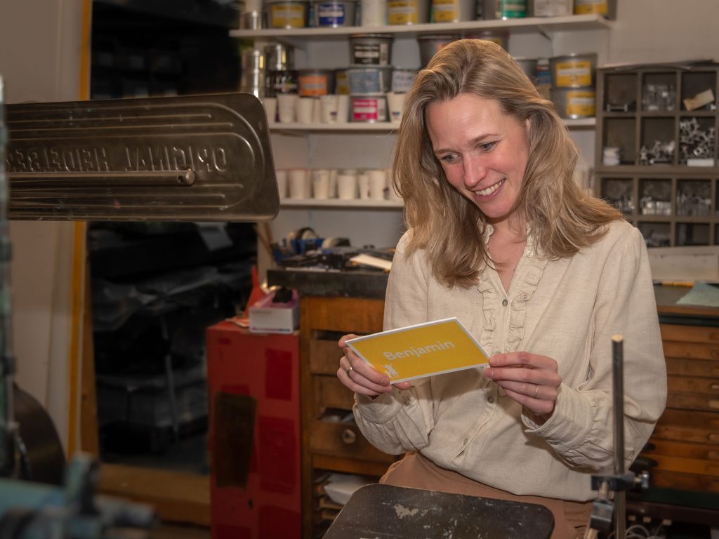 Eline van Miss Letterpress in haar drukkerij in Haarlem met een gele kaart in handen